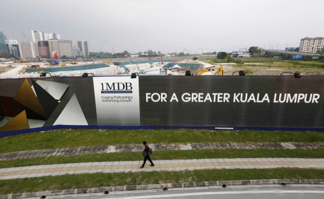 File photo of man walking past a 1 Malaysia Development Berhad billboard at the funds flagship Tun Razak Exchange development in Kuala Lumpur